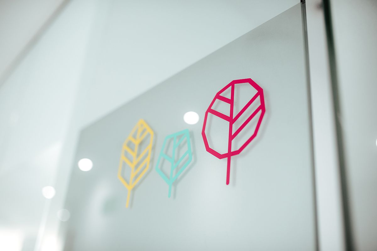 Detalle de los tres árboles del logotipo, amarillo, verde y rosa, sobre el cristal